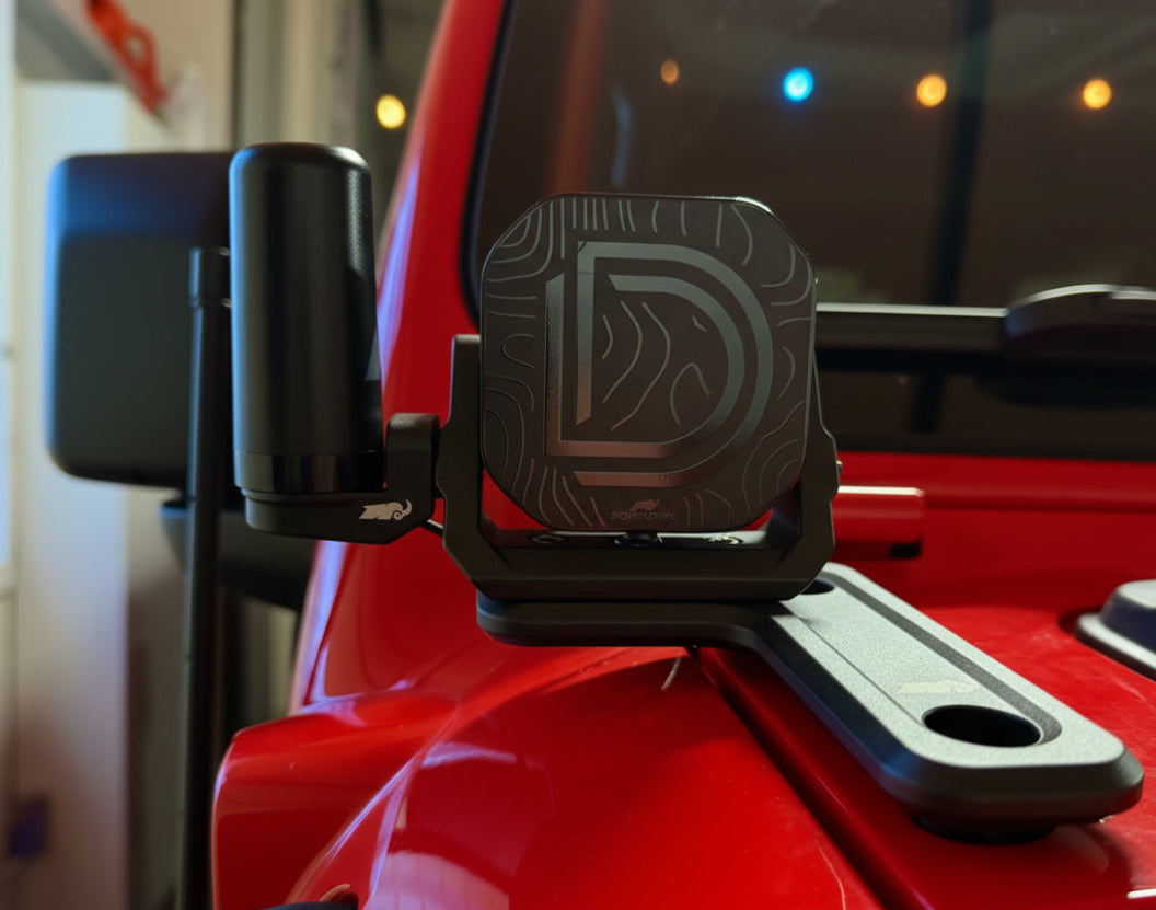 Off road light with black cover and antenna, on a red vehicle.