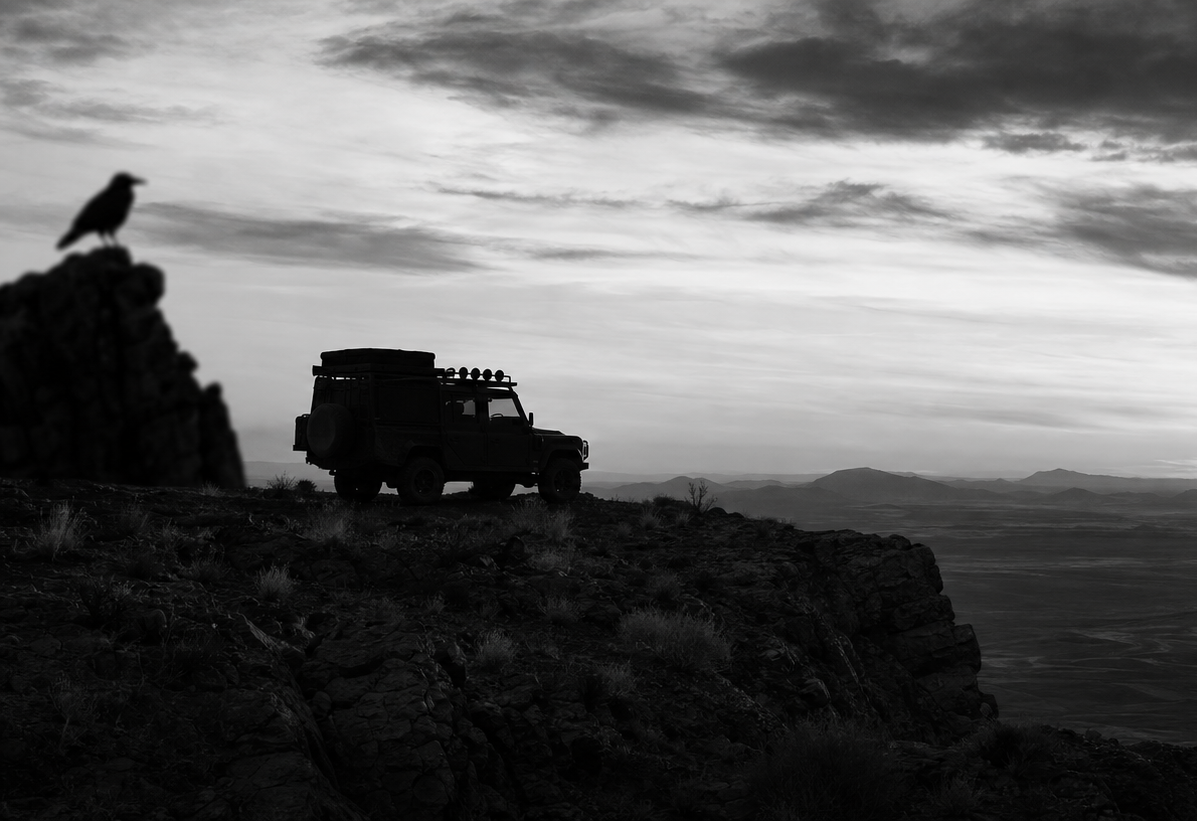 Silhouette of a vehicle on a cliff with a bird and sunset in the background